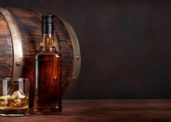 What is Whisky? A poured glass of whisky, next to a whisky bottle, both in front of a whisky cask