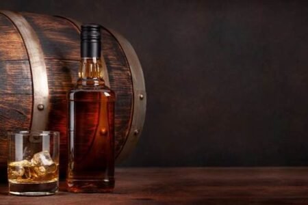 A poured glass of whisky, next to a whisky bottle, both in front of a whisky cask